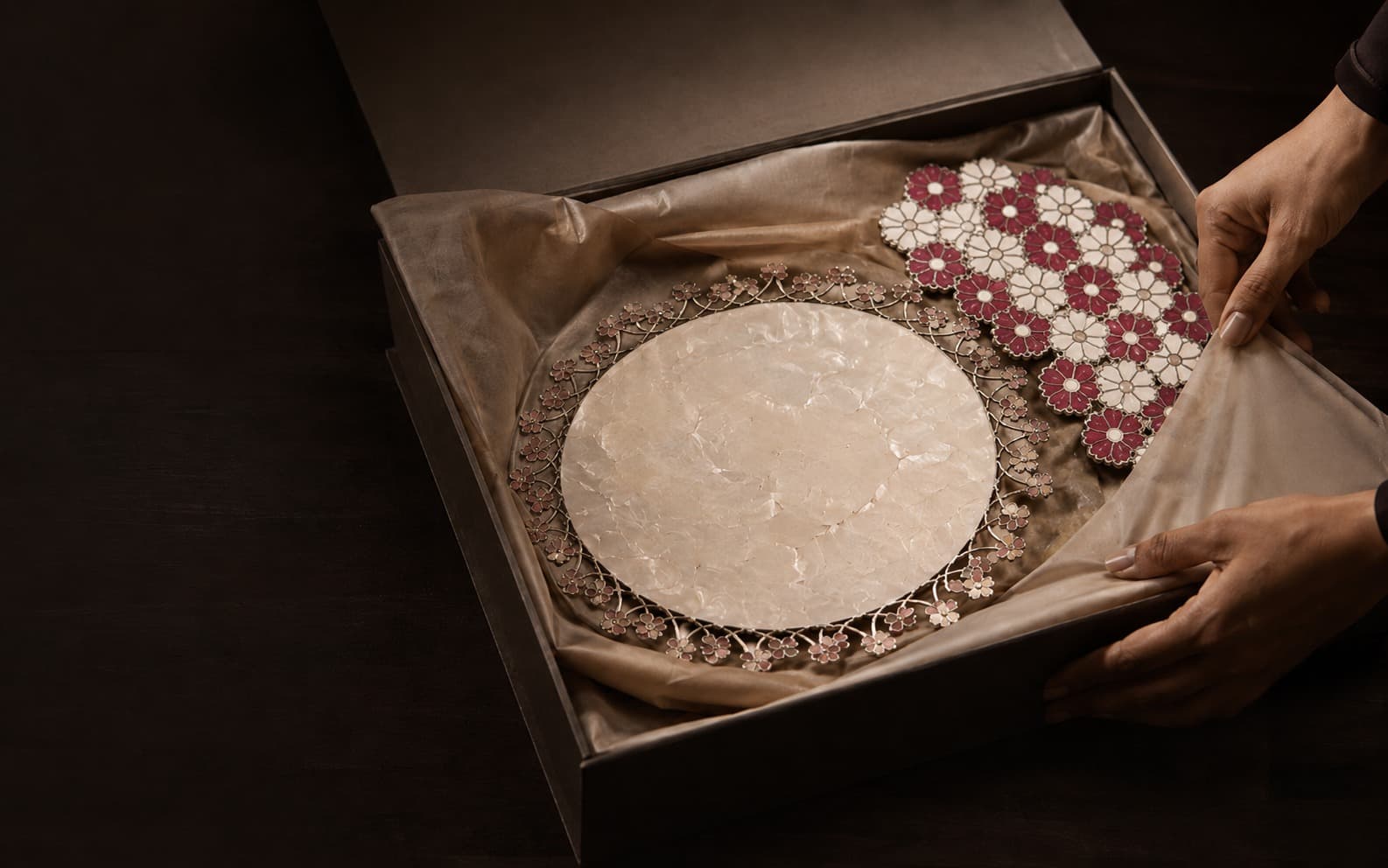 Hands finishing an antique-gold ribbon on a Kanikkae corporate gift, repeated with care across a set